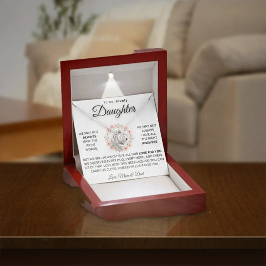 To Our Daughter Love Knot necklace from Mom & Dad in a lit mahogany gift box on a wooden table